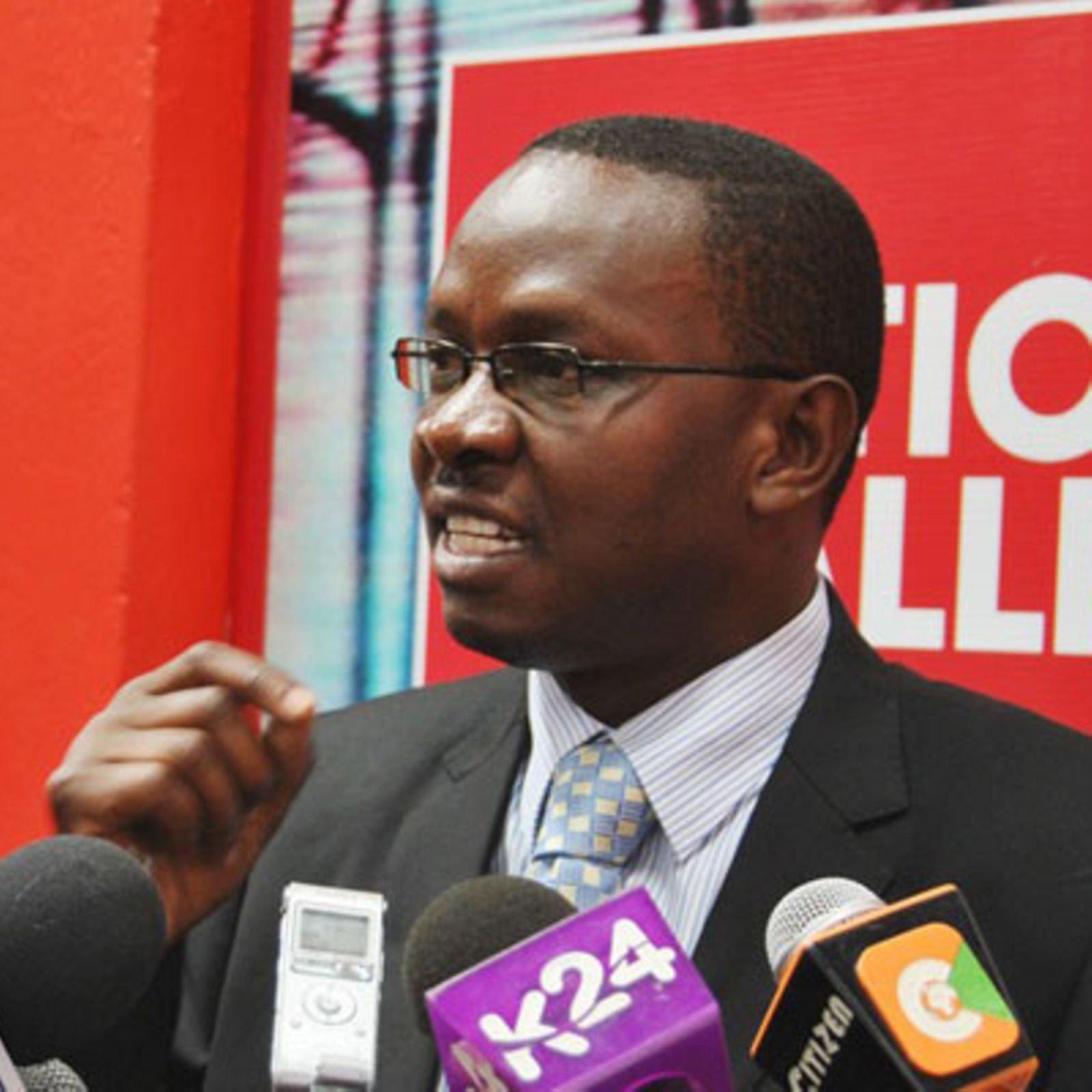 Onyango Oloo speaks into a microphone during a public event.