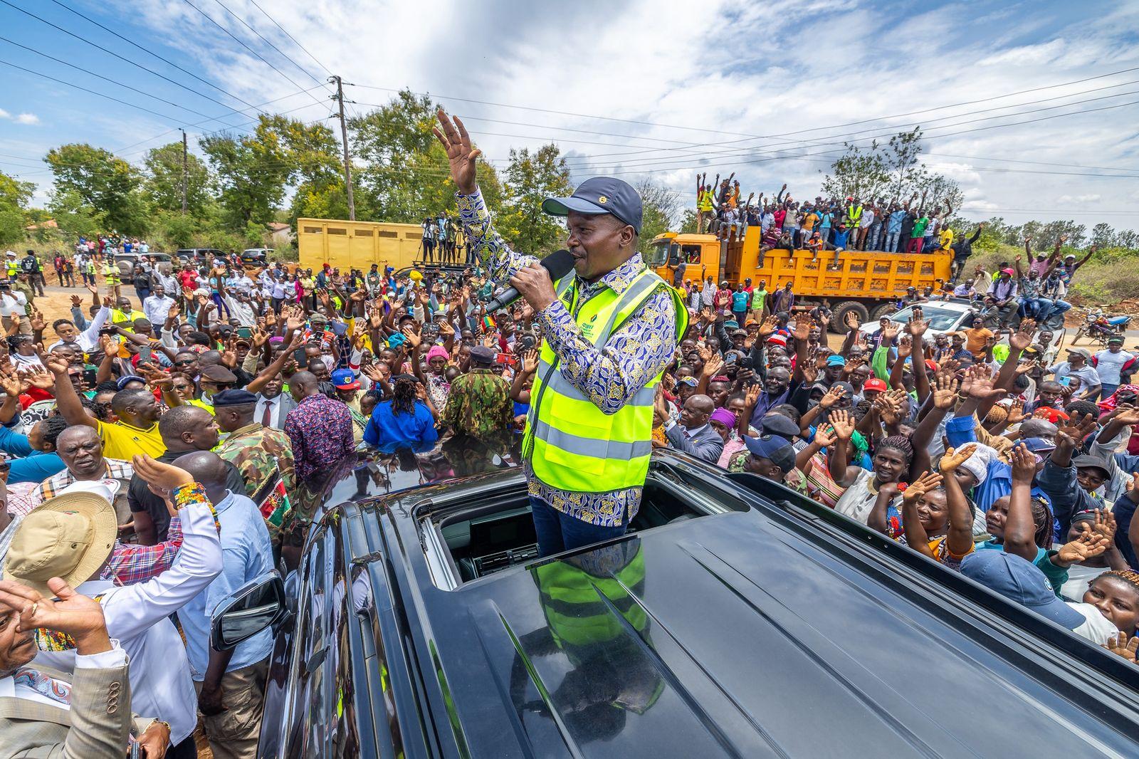 Deputy President Kithure Kindiki addresses residents during a public rally in a yellow cap and reflective vest.