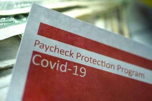 Paycheck Protection Program COVID-19 relief document with US dollar bills in the background.